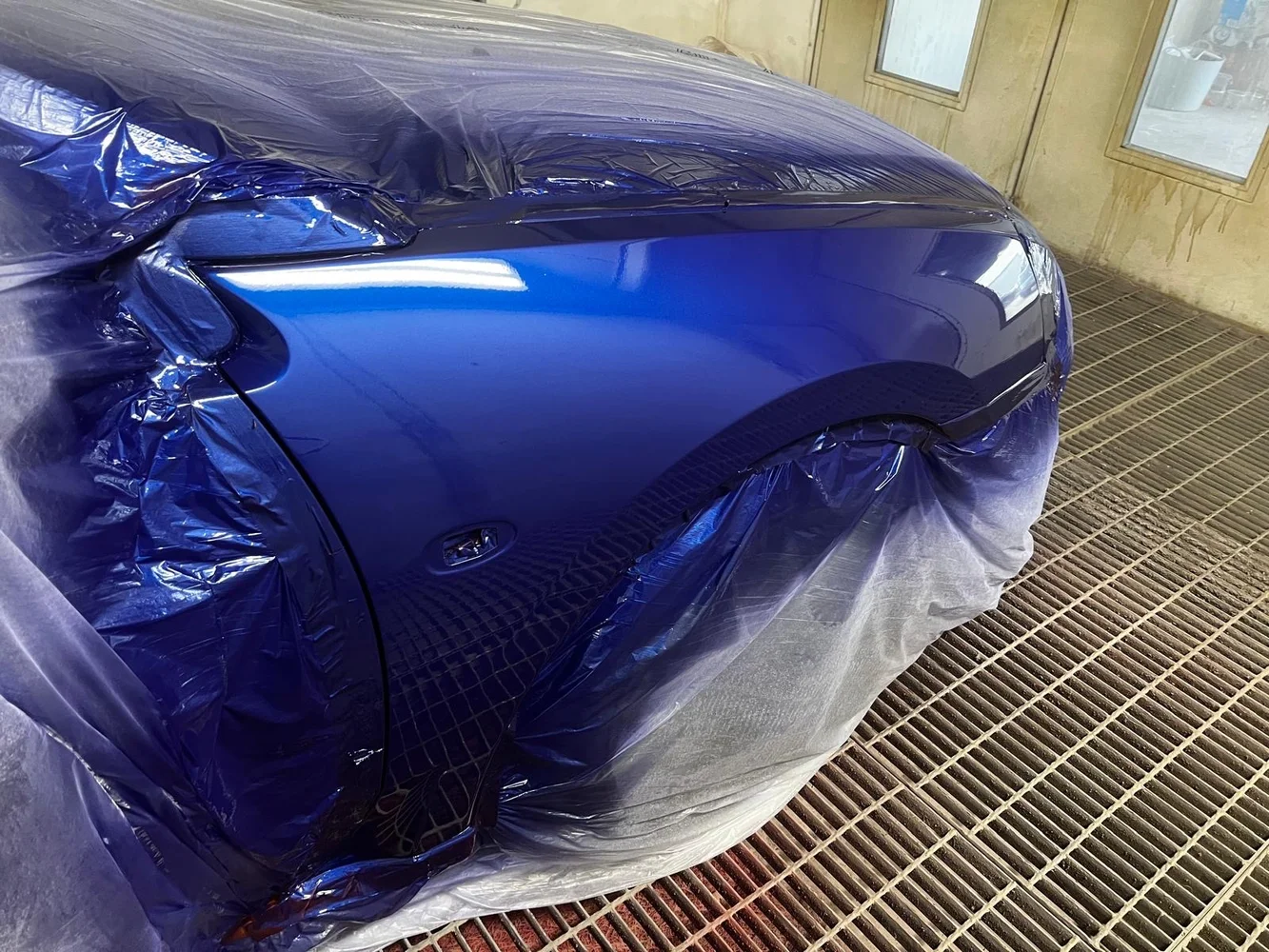Glossy blue vehicle panel after refinishing inside the spray booth